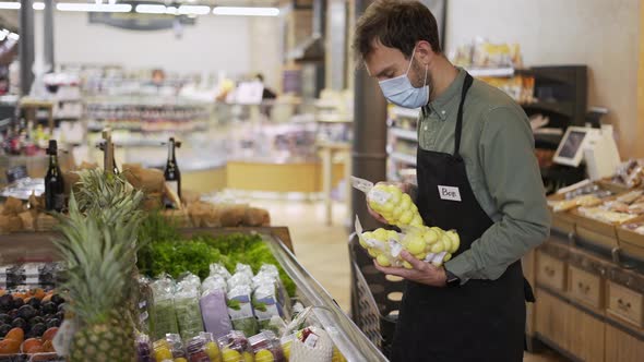 Male Assistant in Supermarket Food Store Worker in Medical Mask and Apron Arranges Packed Products