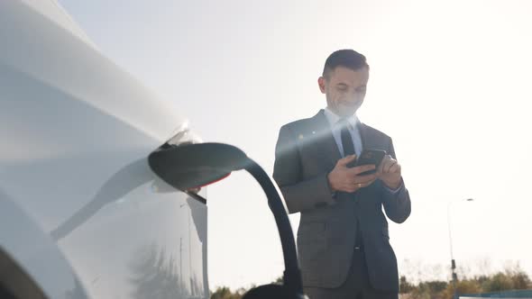 Caucasian Businessman Using Smartphone and Waiting Power Supply Connect to Electric Vehicles 