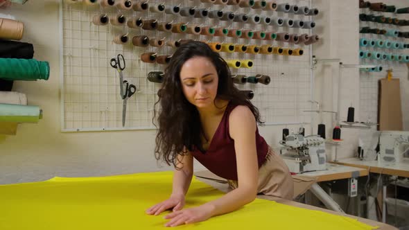 female tailor straightens yellow fabric for work on the table in the studio.