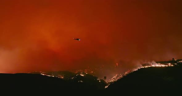 Epic Shot of Helicopter Flying Above Wildfire. Plumes of Orange and Red Flames