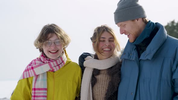 Waist up portrait view of the three young friends chatting with each other while walking in snow