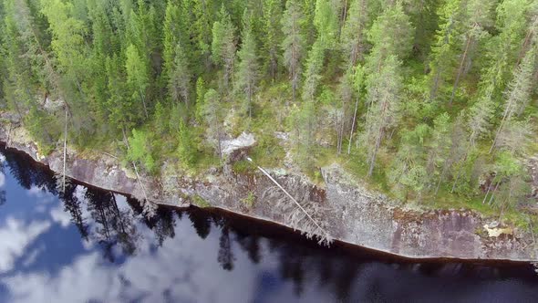 Aerial drone footage of the boreal wilderness. Old fallen pine trees on a steep cliff and mirror sur