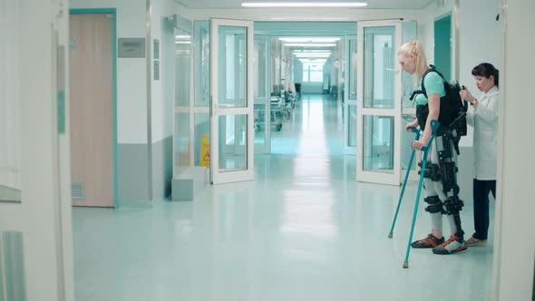 A Woman is Walking Along the Hospital in Exoskeleton with Assistance