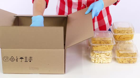 Volunteer in Protective Gloves Packs Pasta in Plastic Containers, Puts Them To Cardboard Box