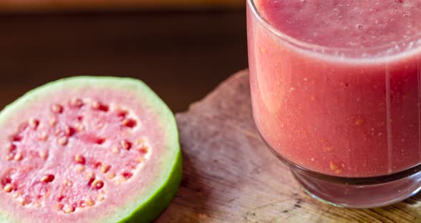 Glass of red guava juice and sliced guava slice on wooden background