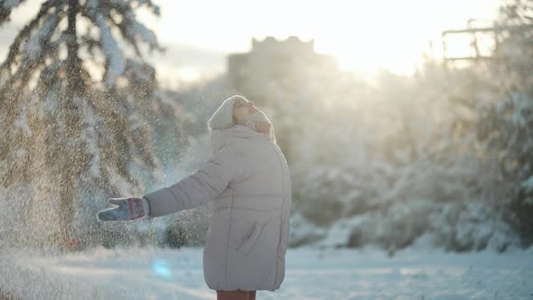 Playful Young Woman in Warm Clothes Throws Snow Up Circles Around Her and Clapping Hands with