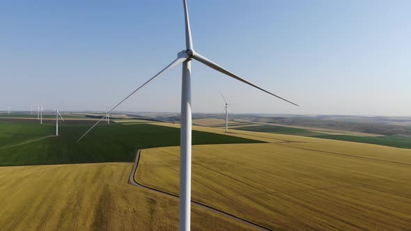 Aerial view raising up revealing static blades of a wind turbine in the middle of agricultural field