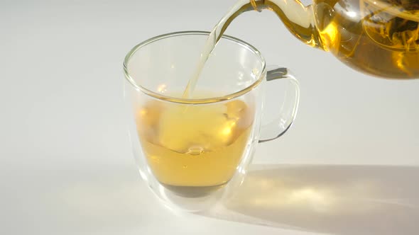 Closeup of Hot Green Tea Pouring to Double Wall Glass Cup From Glass Teapot