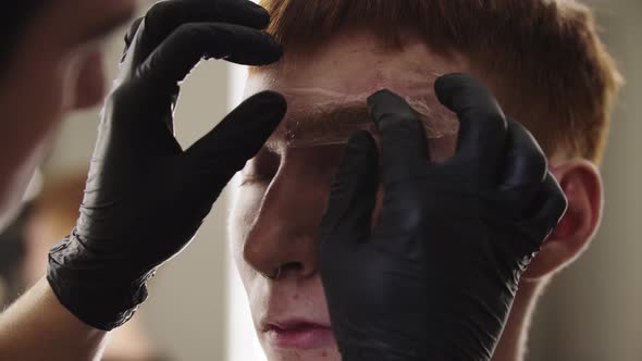 A Man Eyebrow Master Applying the Wrapping on the Eyebrow of His Male Client