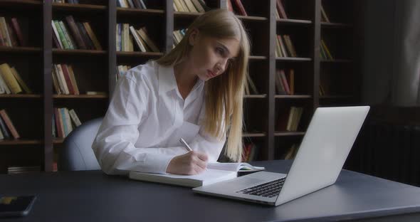 Business Woman is Pensively Writing Notes in Front of a Laptop