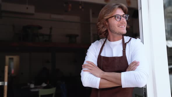 Smiling blond man barista in eyeglasses looking around