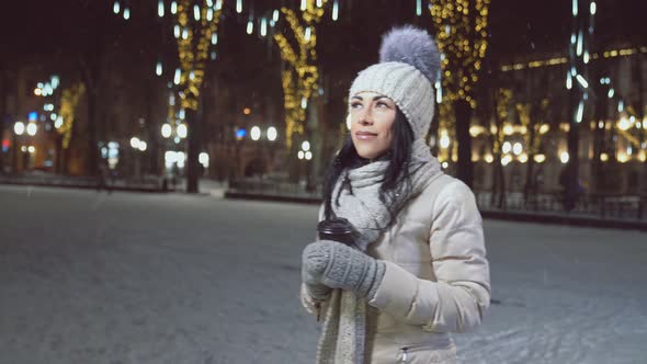 Girl in Warm Clothing with Cup of Coffee on Winter Square