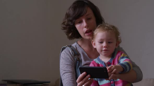 Caucasian woman with baby looking smartphone at home