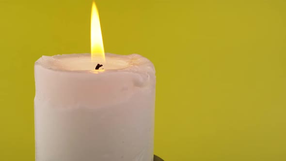 Burning White Candle with a Bright Flame on an Isolated Yellow Background