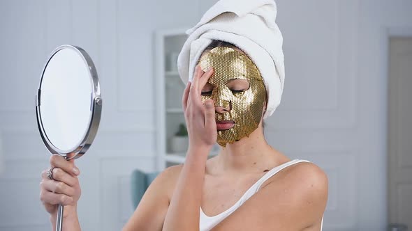Woman Fixing Rejuvenating Cosmetic Golden Tissue Mask on Face