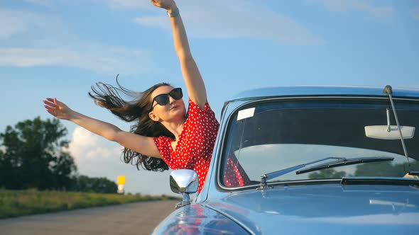 Young Girl in Sunglasses Leaning Out of Vintage Car Window and Enjoying Trip