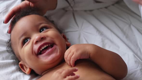 Amused Biracial Toddler Smiling and Laughing with His Parents While Laying Down on the Bed