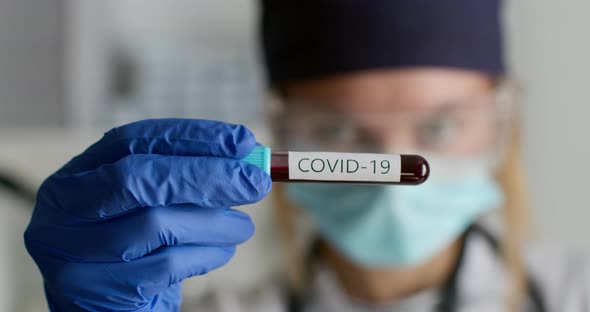 Close-up Shot. A Lab Worker in a Protective Suit Is Showing a Test Tube with the COVID-19