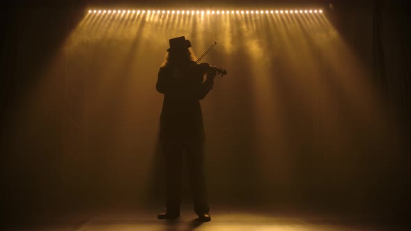 A Silhouetted Violinist Musician with Lush Hair and Wearing a Hat Plays the Classical Wooden Violin