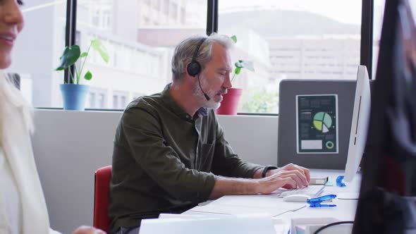 Caucasian businessman sitting using computer talking on phone headset in office