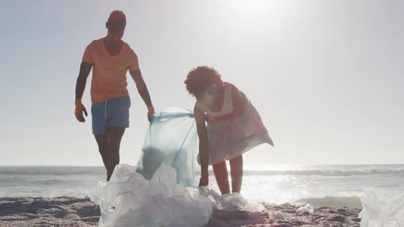 African american couple segregating waste with gloves on sunny beach