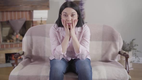 Camera Approaching To Adult Caucasian Woman Sitting with Shocked Facial Expression and Holding Head