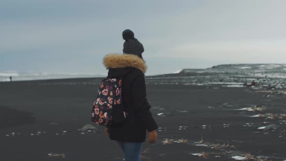 Yong Woman Traveler Walking on Volcanic Black Sand Beach in Iceland