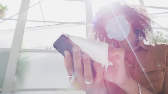 Woman wearing face mask wiping her smartphone with a tissue