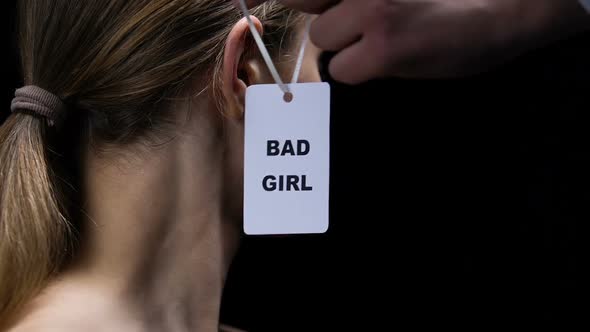 Male Hand Hanging Bad Girl Label on Female Ear, Social Disrespect and Submission