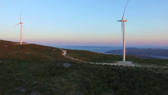 Flying above two elegant white windmills on green hills alt
