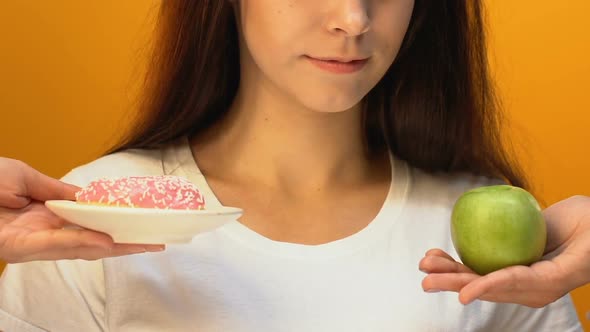 Young Lady Choosing Green Apple Instead of Sweet Donut, Enjoying Juicy Fruit