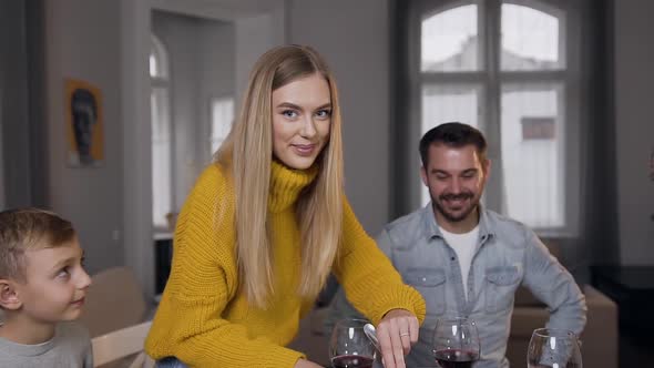 Beautiful Blond Mother in Knitted Yellow Sweater Looking at Camera while Slicing Roast Turkey