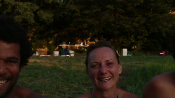 Portrait of group of friends sitting in nature at sunset, laughing at camera