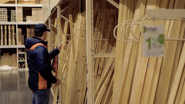 Young Guy Chooses Wooden Beams in Building Materials Store.