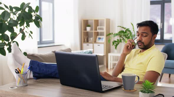 Man with Laptop Calling on Smartphone at Home