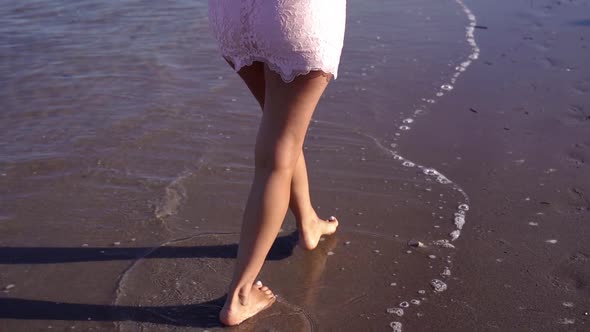 Young Woman in Elegant Dress Walks Along Wet Sandy Beach