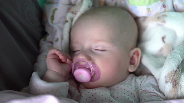 A Baby Is Sleeping with a Pacifier in Its Mouth in a Stroller. Face Close Up