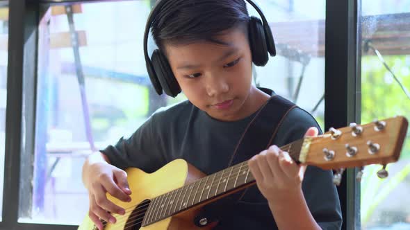 Asian boy learning to play the guitar in virtual meeting for play music online together with friend