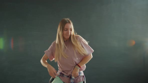 Cute Teenage Blonde Dancing on Dark Stage with Grey Bokeh Background