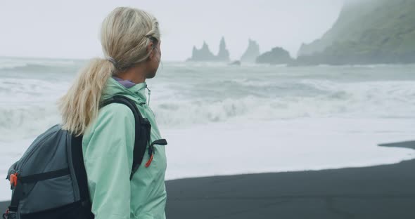 Woman with a Green Raincoat Walking on a Black Sand Beach Enjoying View to Reynisfjara Sea Stack