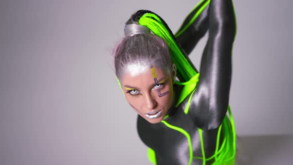 Slim Young Woman with Futuristic Makeup and Zombie Contact Lenses Looking at Camera Bending on Cube