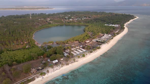 Epic aerial view of Gili Meno during sunlight with golden beach,hotel area and nature lake in backgr