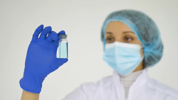 A Medical Worker Shows the Coronavirus Vaccine Wearing Blue Protective Gloves on White Background 