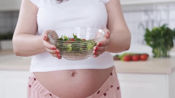 Pregnant Healthy Diet Woman Holds Out Salad with Fresh Vegetables and Herbs Closeup