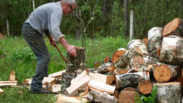 Elderly person is steadily chopping birch logs with an ax