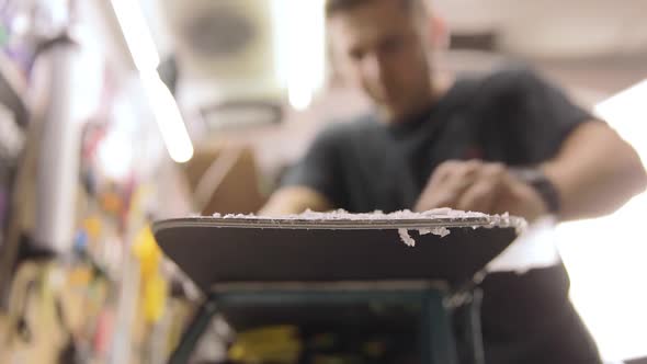 Man Hands With Scraper Scrape The Wax Off The Snowboard. Front View