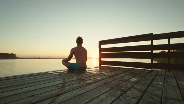 A Young Man is Sitting on the Edge of the Pier and Meditating