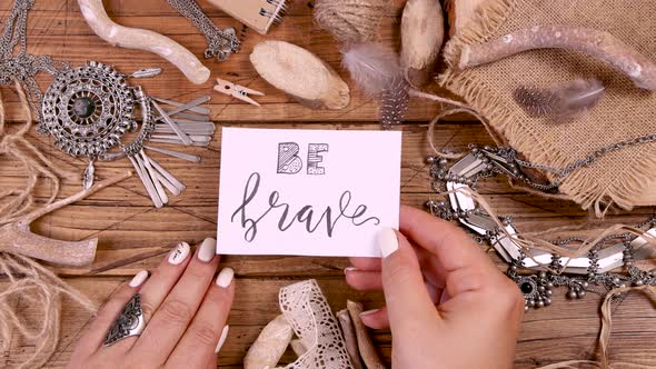 Hand with BE BRAVE card over a wooden table top view