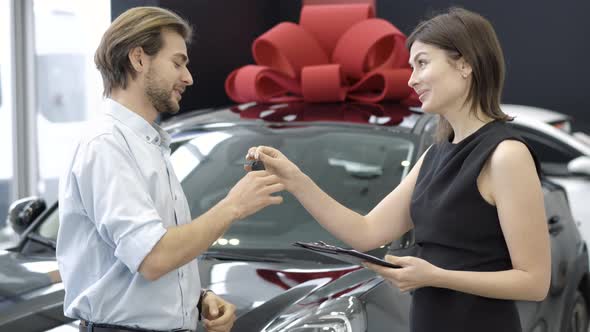 Side View of Smiling Woman Passing Car Keys To Happy New Owner in Dealership. Positive Caucasian
