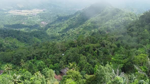 Aerial View Of Lush Hillside Forest In Amed, Bali. Dolly Forward, Tilt Up To Reveal Rolling Clouds